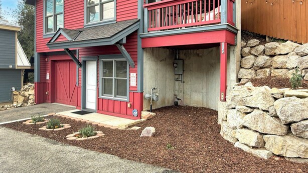 A red two-story house with a balcony, stone wall, and a small garden area.