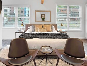 Une chambre à coucher comprenant un lit, deux tables de chevet, une petite table d’appoint, une chaise et une petite table avec un magazine.