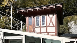 A chalet with a glass balcony, metal railings, and a view of a forested hillside. - Nachtigall Apartment at Schlössle Seeburg – Stylish Comfort in the Swabian Jura (Bad Urach)