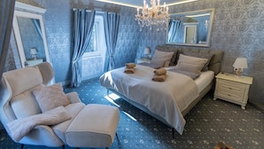A bedroom with a large bed, a sitting chair, a nightstand, a mirror, and a chandelier. - Nachtigall Apartment at Schlössle Seeburg – Stylish Comfort in the Swabian Jura (Bad Urach)
