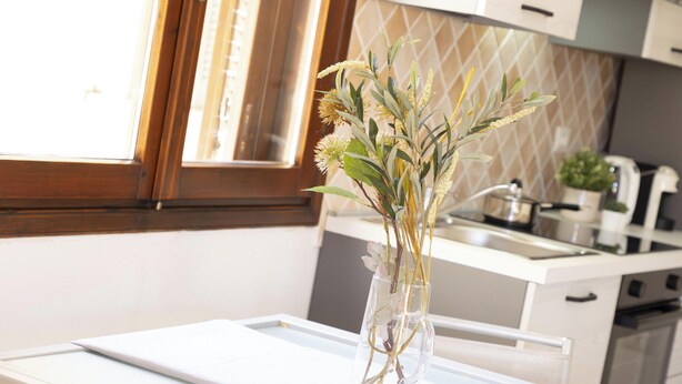 A kitchen with a window, a sink, and a vase with dried plants on the counter. - Studio Aura by Propertize - centro Olbia (Olbia)