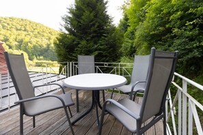 Eine Terrasse mit einem runden Tisch und vier Stühlen, umgeben von einem weißen Geländer, mit Blick auf einen bewaldeten Hang.