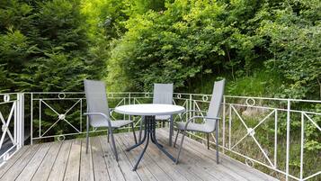 Eine Holzterrasse mit einem runden Tisch und zwei Stühlen, umgeben von einem weißen Metallgeländer.