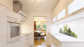 A modern kitchen with white cabinetry, a built-in oven, and a window overlooking a garden.