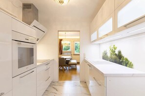 Eine moderne Küche mit weißen Schränken, einem Einbauofen und einem Fenster mit Blick auf einen Garten.