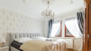 A bedroom with a bed, a nightstand, a chandelier, a window with curtains, and patterned wallpaper.