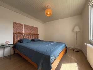 Un dormitorio con una cama, una mesita de noche, una lámpara de pie, un radiador y una ventana.