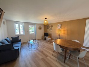 Una sala de estar con sofá, una mesa de centro, una mesa de comedor con sillas, un televisor y una lámpara.