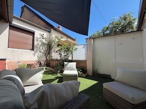 Eine Terrasse mit Gartenmöbeln, ein kleiner Garten und eine weiße Mauer.