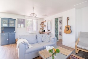 Ein Wohnzimmer mit einer Couch, einem Couchtisch mit Blumen, einer Gitarre und einem Bücherregal.