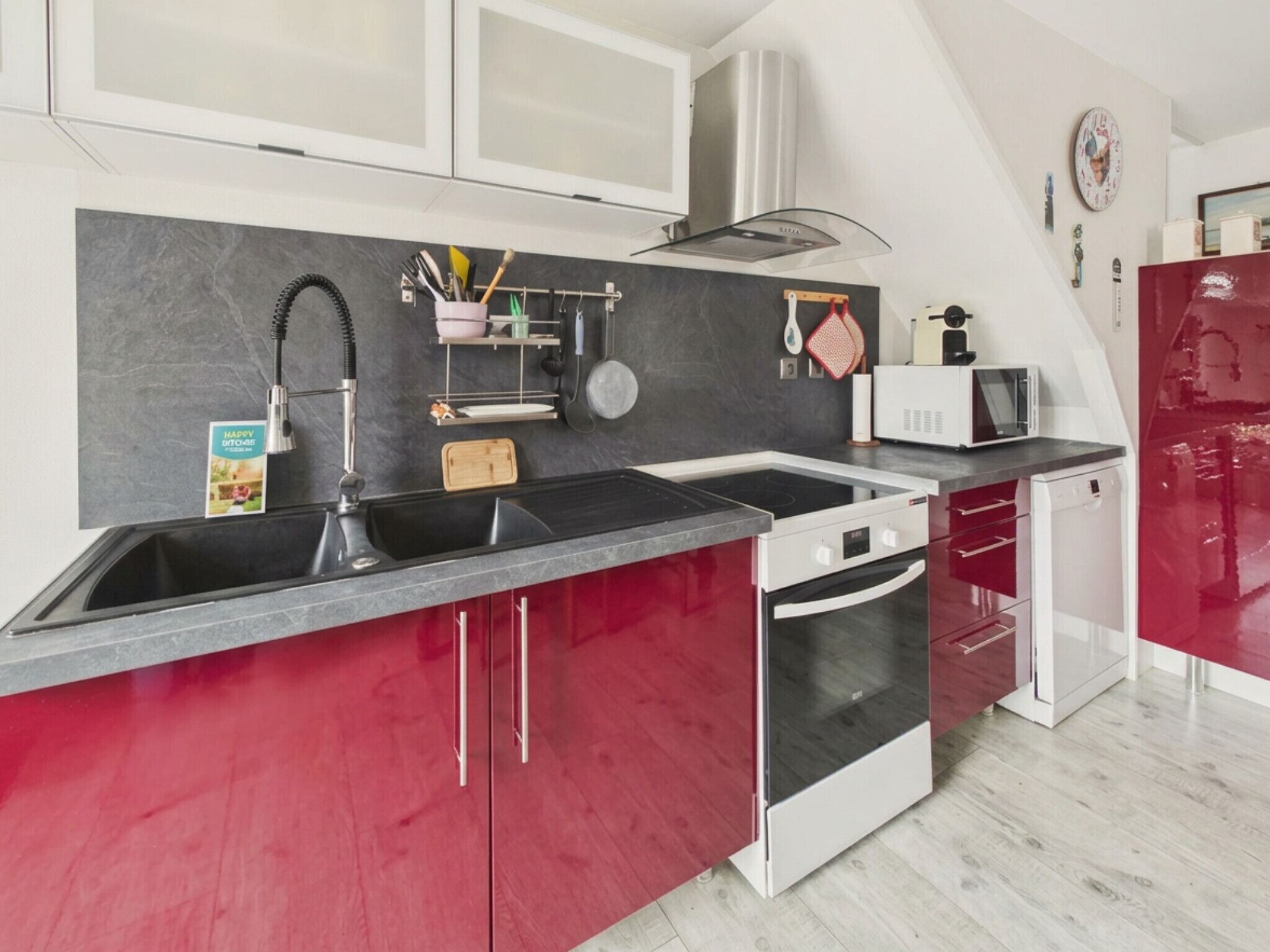 Une cuisine moderne aux couleurs noir et rouge, dotée d’appareils électroménagers en acier inoxydable et d’un four à micro-ondes.