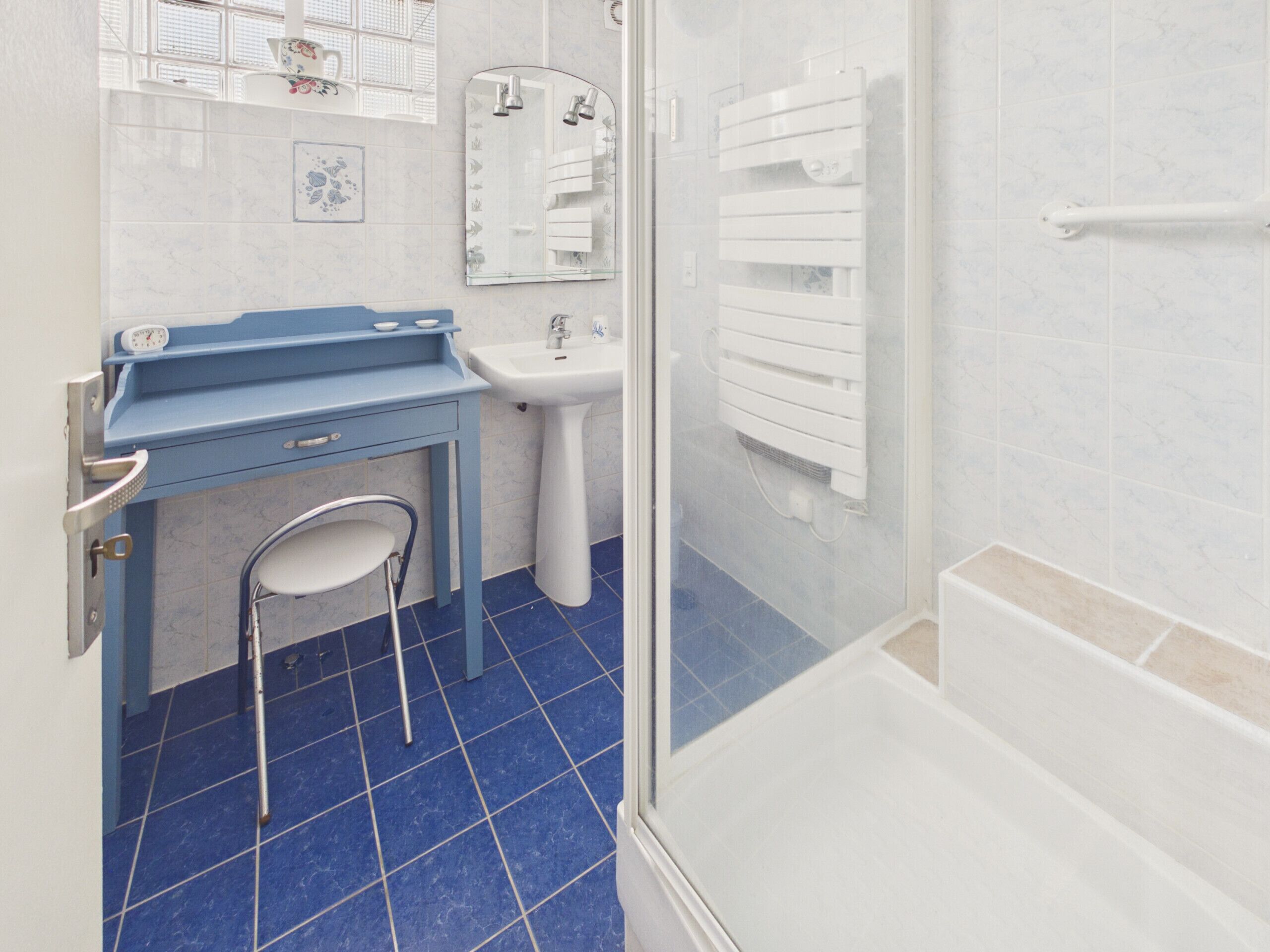Un baño con piso de azulejos azules, un lavamanos, un espejo, un inodoro y una zona de ducha.