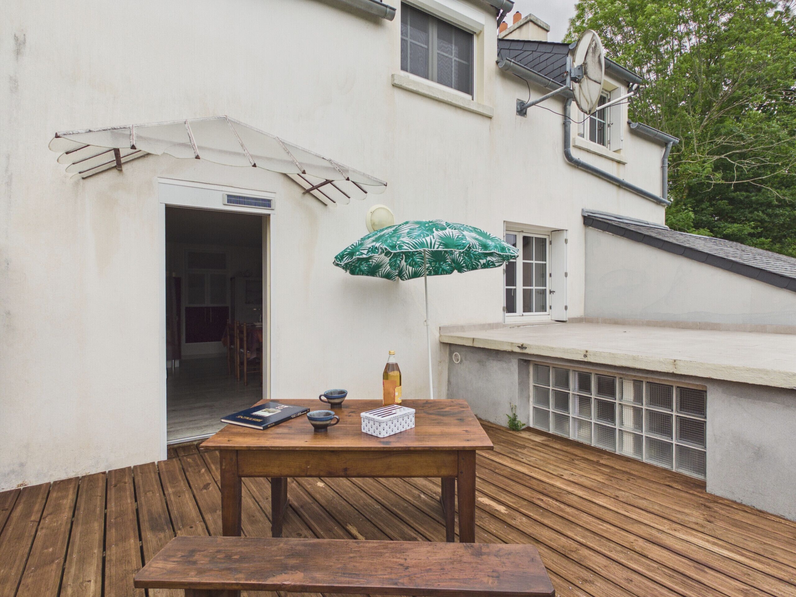 A wooden deck with a table and bench, a green umbrella, and a bottle.