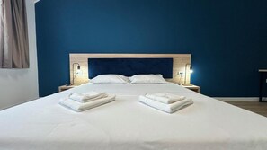 A neatly made bed with two folded towels, a wooden headboard, bedside lamps, and a blue wall. - Eliza Apartments - free parking - by NEO (Timișoara)