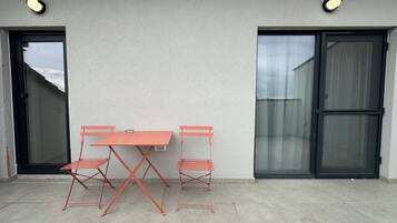 Een terras met een tafel en twee stoelen, een schuifpui en een wandlamp.