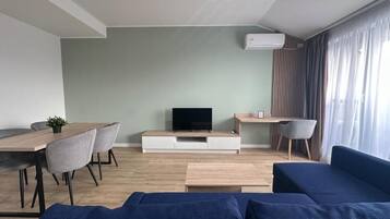 Ein modernes Wohnzimmer mit Fernseher, Sofa, Esstisch und Stühlen.