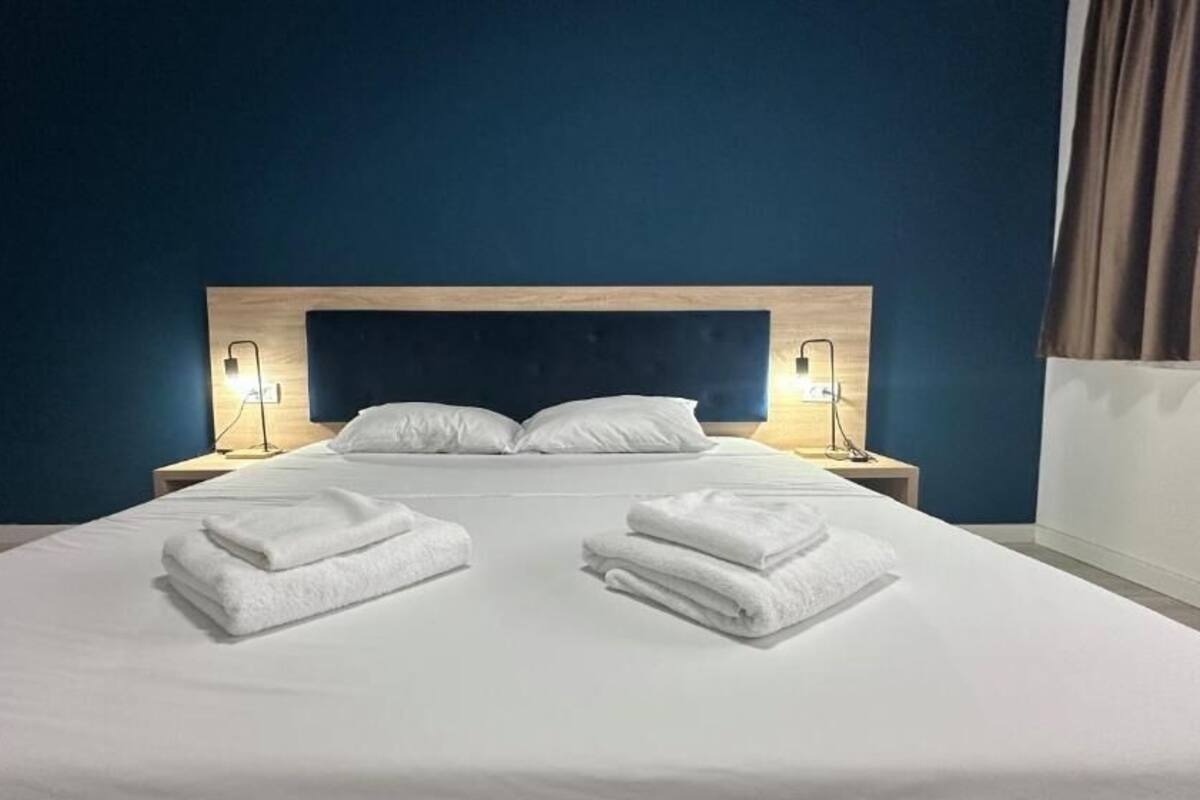 A hotel room with a bed, two bedside lamps, and folded towels on the bed.
