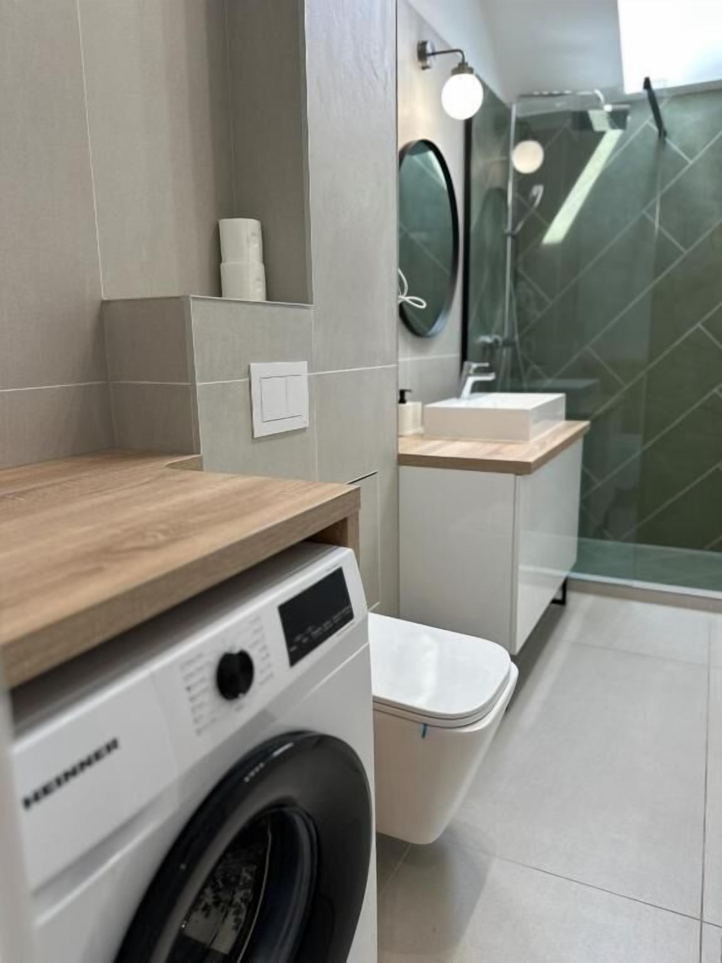 A modern bathroom with a washing machine, toilet, and glass shower enclosure.