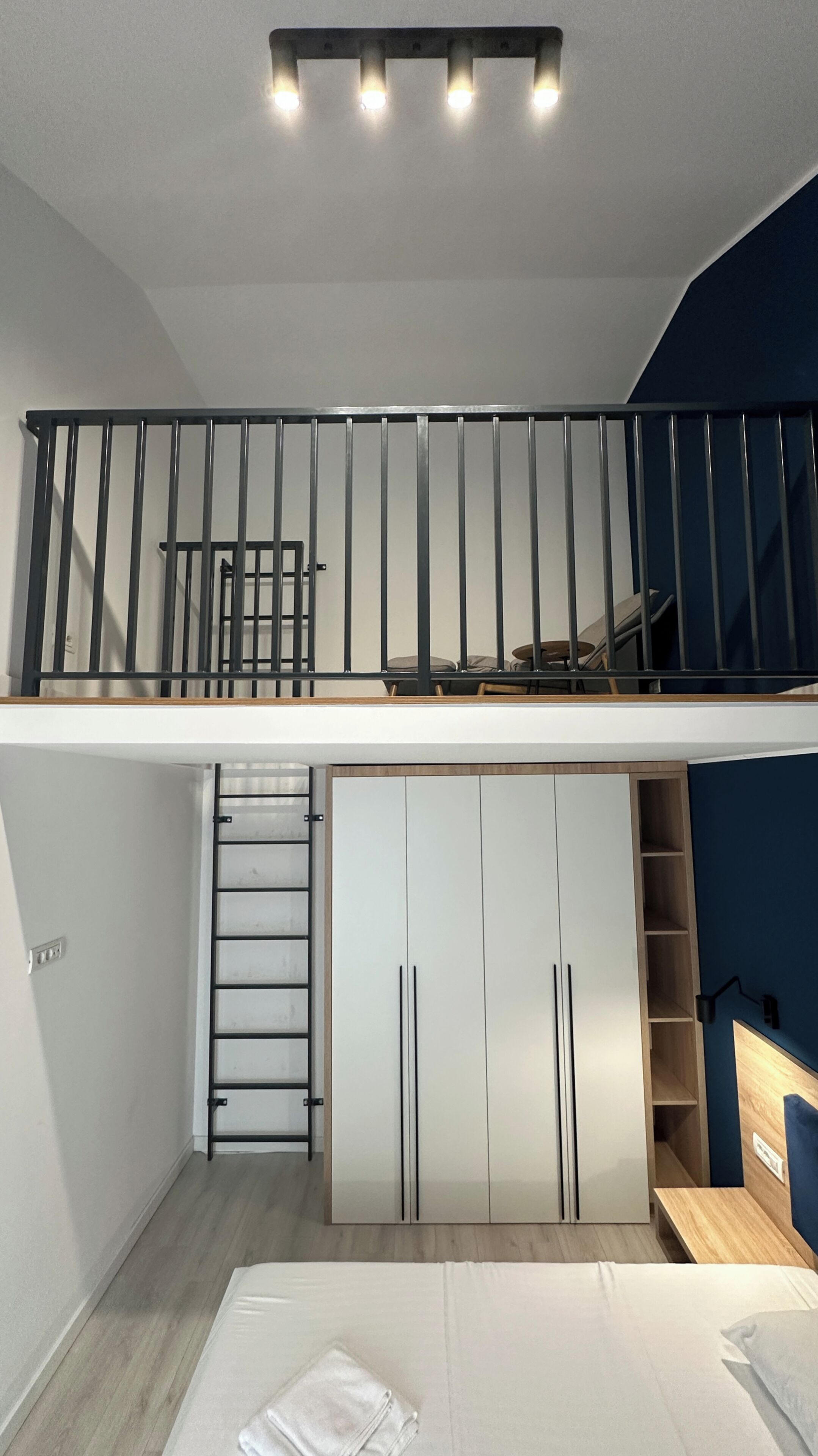 A loft bedroom with a mezzanine, a staircase, a wardrobe, and a bed.