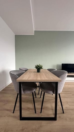 Uma sala de jantar moderna com mesa de madeira, pés de metal preto e cadeiras estofadas em cinza.