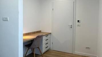 Una habitación con piso de madera, un escritorio con silla, una puerta blanca y una lámpara en el techo.