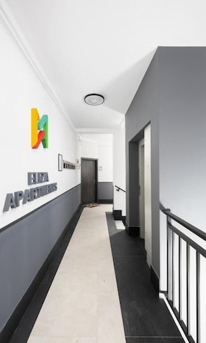 Ein Flur mit einem Schild, auf dem 'ELIZA APARTMENTS' steht, einer schwarzen Geländer und einer Tür am Ende.