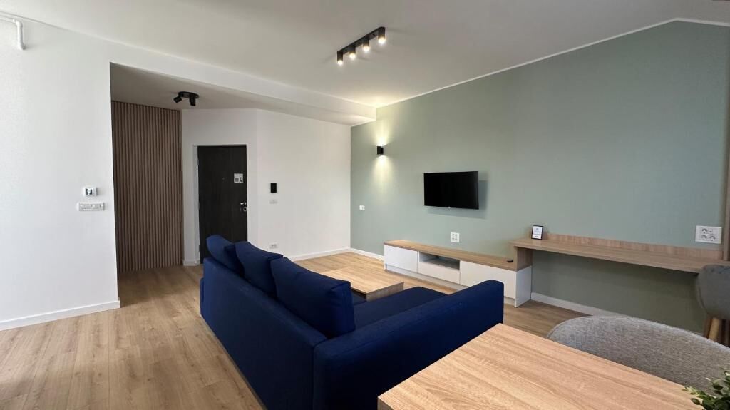 A modern living room with a sofa, a coffee table, a TV mounted on the wall, and a wooden floor.