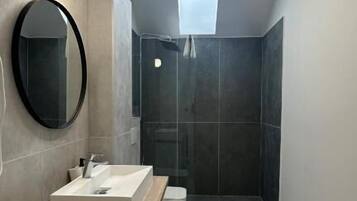 A modern bathroom with a wooden vanity, a round mirror, a shower area, and a skylight.