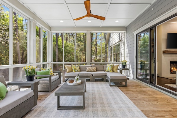 A covered outdoor living area with a ceiling fan, large windows, and a sofa set. - Sunset Rentals | 38 Governors Lane (Hilton Head Island)