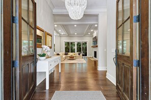 A spacious hallway leading to a living area with a chandelier, wooden floors, and a white console table with a plant. - Sunset Rentals | 38 Governors Lane (Hilton Head Island)