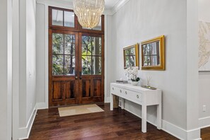A wooden door, white console table, and a chandelier in a hallway. - Sunset Rentals | 38 Governors Lane (Hilton Head Island)