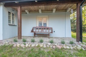 Un porche cubierto con un banco de madera, una ventana con cortinas y un sendero de piedra.