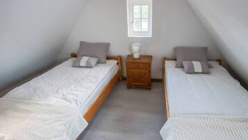 Quarto com duas camas de solteiro, uma mesinha de cabeceira de madeira, uma janela e um abajur branco.