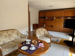 A living room with a sofa, armchair, and a round coffee table set with plates, cups, and a teapot. - Terrace Apartment in the Harz with Mountain View, Private Terrace, and Wi-Fi (Bad Harzburg)