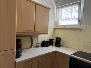 A kitchen with wooden cabinets, a window with a decorative curtain, a coffee maker, and a toaster. - Terrace Apartment in the Harz with Mountain View, Private Terrace, and Wi-Fi (Bad Harzburg)