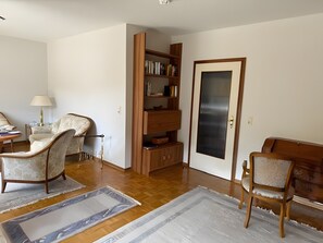 A living room with a wooden bookshelf, two armchairs, a lamp, and a door with a glass panel. - Terrace Apartment in the Harz with Mountain View, Private Terrace, and Wi-Fi (Bad Harzburg)
