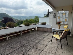 En takterrass med ett bord och stolar, en satellitantenn och utsikt över det omgivande landskapet.