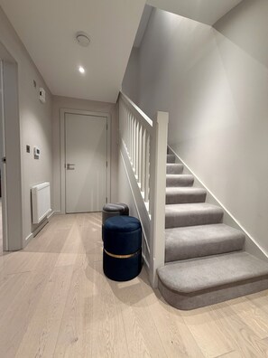 Uma escadaria moderna com corrimão branco, piso coberto por carpete cinza e uma porta no topo.