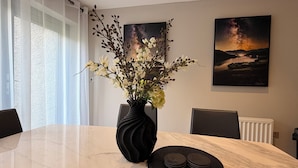 A dining area with a marble table, a black vase with flowers, and two framed landscape paintings. - The Ironworks (Ulverston)