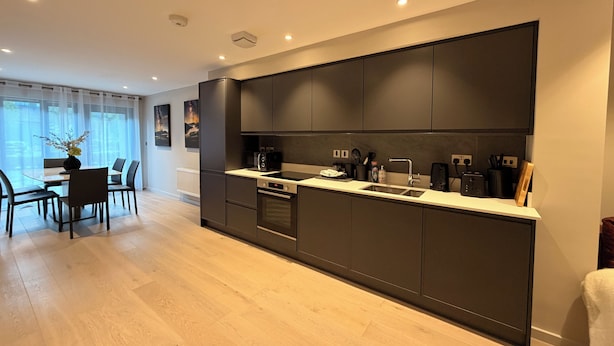 A modern kitchen with dark cabinetry, a built-in oven, and a countertop with a sink. - The Ironworks (Ulverston)