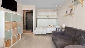 A modern bedroom with a bed, a grey sofa, a TV mounted on the wall, and a built-in wardrobe. - Sunny Studio with a Balcony | Gdańsk | Close to Nature (Gdańsk)