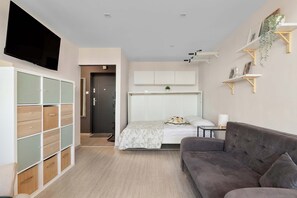 Ein modernes Schlafzimmer mit einem Bett, einem grauen Sofa, einem an der Wand montierten Fernseher und einem Einbauschrank.