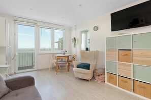 Ein Zimmer mit Esstisch, Stühlen, einer Couch, einem Fernseher und einem Schrank.