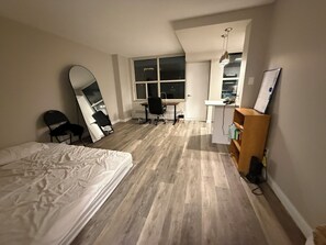 A bedroom with a bed, a desk, a chair, a large mirror, and a wooden shelf.