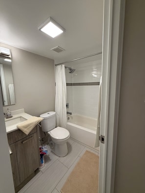A bathroom with a toilet, sink, shower, and a mirror.