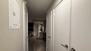 Un pasillo con puertas blancas, una zona de cocina al fondo y suelo de madera.