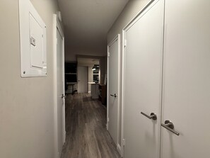 A hallway with white doors, a kitchen area in the background, and a wooden floor.
