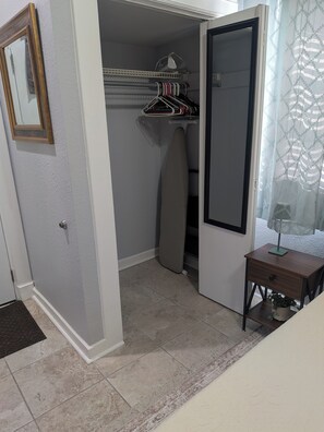 Quarto com guarda-roupa, espelho, uma pequena mesa com uma planta e chão de azulejos.