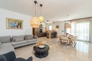 A modern living room with a grey sofa, a round coffee table, and a dining area with a table and chairs.