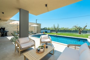 A poolside area with lounge chairs, a table with drinks, and a barbecue grill.